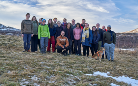 The photo shows a group of participants posing for a group photo in the countryside